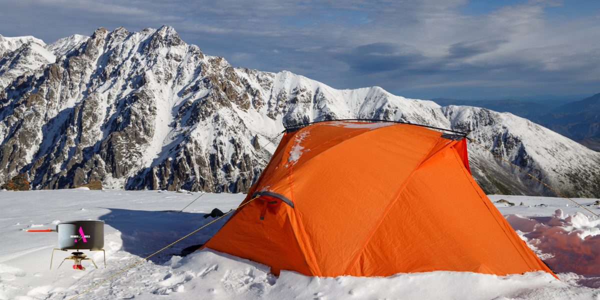 An orange tent on the mountainside with a BbA gas stove next to it